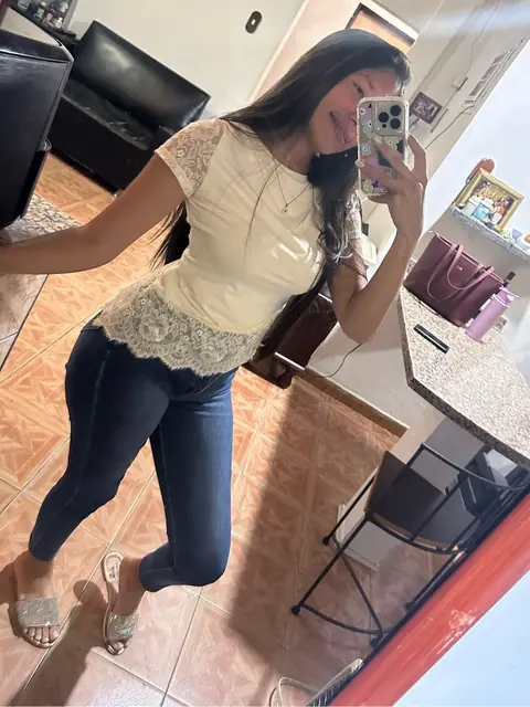 Woman in jeans and a cream lace top taking a mirror selfie